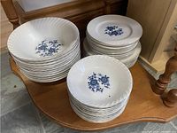 Stacked large bowls, dinner plates, and salad plates all featuring a central blue floral pattern on white ceramic.