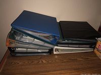 Stack of five binders holding assorted sports cards, unopened showing blue, black, and white covers.