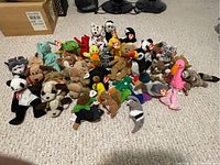 Photo showing a front view of over 30 Beanie Babies plush toys arranged on carpet with various animals like panda, flamingo, frog, duck, and more.