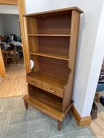 Front view of vintage wooden cabinet showing two open shelves and two side-by-side drawers with wooden handles, standing on four legs.