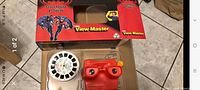 Photo of the Batman & Robin View-Master in red with one reel inserted, alongside the other reel and original box showing graphics and branding.