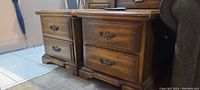 Two wooden nightstands, side by side, showing drawer fronts and decorative handles