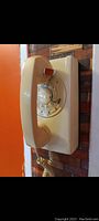 Side angle view of vintage rotary dial telephone mounted on wall, showing handset and rotary dial clearly.
