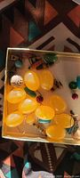 Photo showing close-up of yellow lemon-shaped plastic containers, beads in various colors, and miniature decorative items in a box.