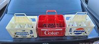 Photo of three vintage plastic beverage crates on a car trunk: one red Coke family pack crate in the center, two cream-colored Kitchener Beverages crates on either side, one showing Pepsi branding.