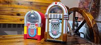 Two vintage desktop jukebox replicas shown together on wooden surface.