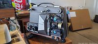 Front and side angle of vintage Revere Model 80 reel to reel movie projector with visible mechanical knobs and lens area, showing aging and wear.