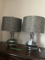 Two matching bedside lamps placed on a wooden surface, showing overall view including shades and bases.