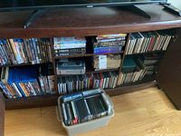Wide view of wooden shelf showing DVDs, CDs, portable radio, and bin with additional CDs.