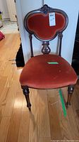 Front view of antique wooden chair with reddish-orange cushioned seat and backrest, showing overall condition and design.