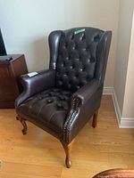 Front view of brown leather wingback chair with button tufting and nailhead trim