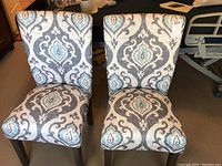 Two matching upholstered high back chairs with damask fabric showing grey, blue, and cream colors, one photo shows both chairs side by side.