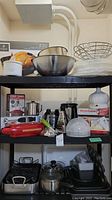 Shelving with metal mixing bowls, wire basket, cake tray, KitchenAid hand mixer, KitchenAid meatloaf pan, Cuisinart blender and hand blender, small grater, and other kitchen appliances and tools.