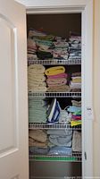 Wide view of shelving with stacks of towels, sheets, and an iron on wire shelves
