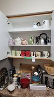 Cabinet with shelves containing coffee mugs in various colors and sizes, teapots, kettle, French press
