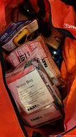 Photo showing orange wheeled tote containing packaged first aid kits with bandages, wipes, and a water bag labeled FAST.