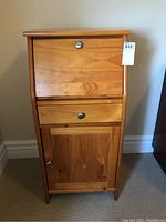 Front view of small wooden secretary desk showing closed drop front compartment, single drawer, and lower cupboard door with metal knobs