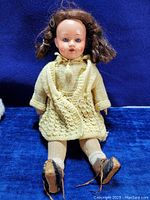 Full view of antique Herm Steiner doll sitting, showing yellow knit dress, boots, and hair condition.