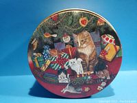 Top view of the round tin canister lid showing colorful Christmas illustration with cats, presents, and tree ornaments.