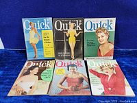 Photo showing full lot of six vintage Quick magazines from the 1950s, arranged in two rows of three on blue fabric background.