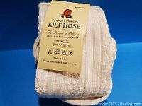 Folded cream colored kilt hose socks with label showing material composition, size medium, hand linked by The House of Edgar made in UK.