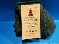 Close-up of the tag on folded green kilt hose showing brand, material composition, size large, and made in UK.