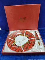Open red box with satin lining displaying cake plate and spatula server neatly tied with white ribbon, showing full holiday pattern detail