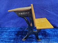 Side view of miniature school desk showing wood surfaces and black cast iron legs with 'SMARTS' embossed.