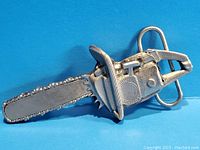 Front view of vintage chainsaw belt buckle showing detailed features and length.