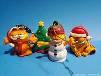 Front view of four Garfield and Christmas themed vinyl figures including Garfield with scarf and ear muffs, snowman Garfield, Santa Garfield, and a Christmas tree ornament