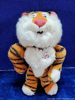Front view of plush tiger toy showing full body with striped orange and black fur, white chest and face, pink nose, and Esso patch on chest