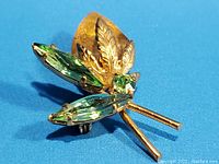 Close-up image of vintage floral leaf brooch showing navette-cut light green peridot rhinestones and detailed gold-tone metal leaves.