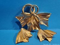 Gold tone brooch with flowing leaf and ribbon design against blue background