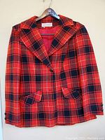 Front view of red tartan patterned jacket showing lapel collar, two front flap pockets, and button closure.