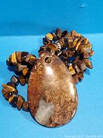 Photo showing large tiger eye pendant with polished surface and natural brown and gold patterns against blue background.