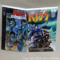 Two comic books shown side by side: KISS Psycho Circus #16 and KISS World Without Heroes #2, both with colorful fantasy/science fiction covers.