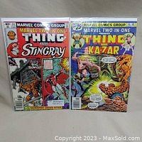 Photo of Marvel Two-in-One comic books #64 and #16 showing front covers with The Thing, Stingray, Ka-Zar, and a dinosaur character.