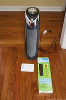 Photo of the Germ Guardian black tower air purifier with power cord, new HEPA filter box, and printed instructions on floor.