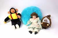 Three dolls including a large monkey plush, vintage porcelain doll, small brown plush doll, and a fluffy blue round pillow.
