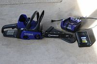 Chainsaw, battery, charger and chain cover laid out on concrete floor