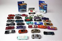Wide view of over 30 Hot Wheels toy cars laid out in rows, mostly loose, showing a variety of colors and models