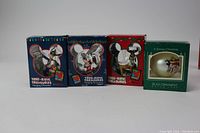 Four boxed Disney Christmas ornaments arranged in a row showing the front of the boxes with Mickey Mouse head-shaped windows