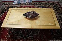 Top view showing rectangular maple table top with decorative black inlay border and geometric sunburst pattern in wood grain.