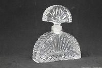 Clear crystal perfume bottle with fan cut stopper against a black background highlighting its shape and detailed cut pattern.