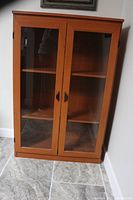 Front view of redwood display cabinet with two glass doors and black handles, standing on tiled floor.