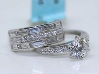 Close-up photo of engagement and wedding rings showing round main stone and accent diamonds with sterling silver bands.