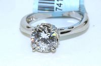 Close-up image of the sterling silver engagement ring showing the round clear center stone set on a polished band with four prongs, tag visible