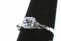 Sterling silver engagement ring with radiant cut clear simulant diamond shown at an angle emphasizing the stone and band details on black display.