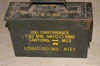 Front-diagonal view of vintage green U.S. Military metal ammo box with yellow stencil text showing cartridge specifications and condition