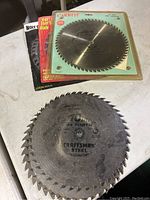 Saw blades including Craftsman Steel and Carbitip blades on table, some loose and one in original packaging.